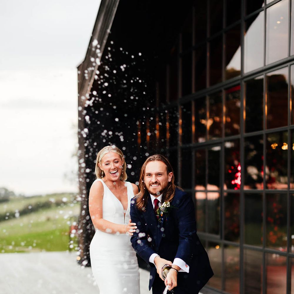 Bride and groom pop champagne together to celebrate their autumn wedding 