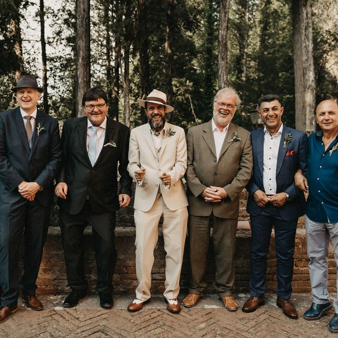 The groom and groomsmen line up in neutral toned olive green and blue suits