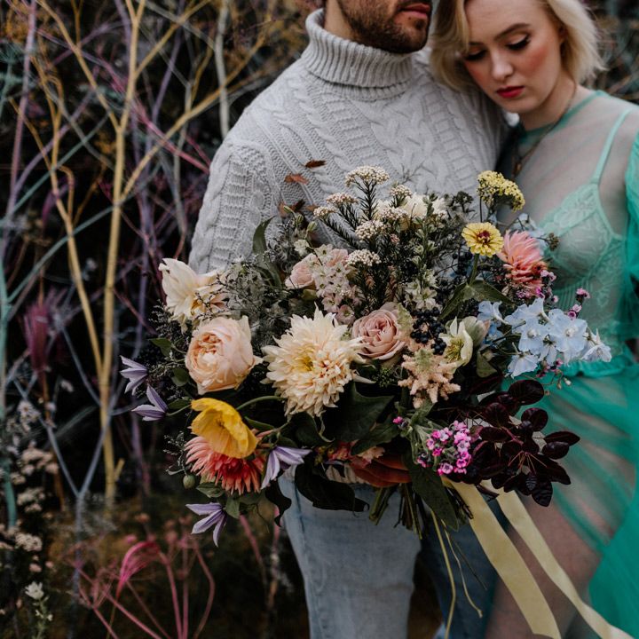 Groom in a grey cable jumper holding a colourful flower wedding bouquet tied with ribbon 
