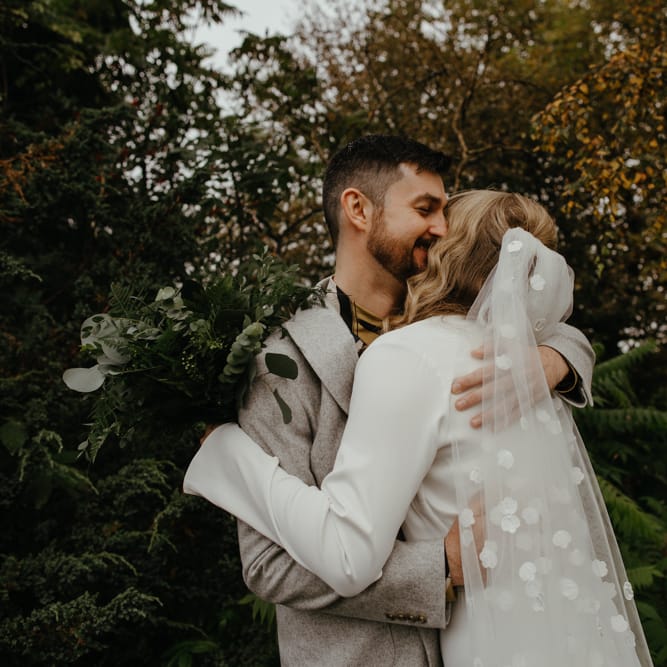 Groom embracing his bride in a appliqué wedding veil
