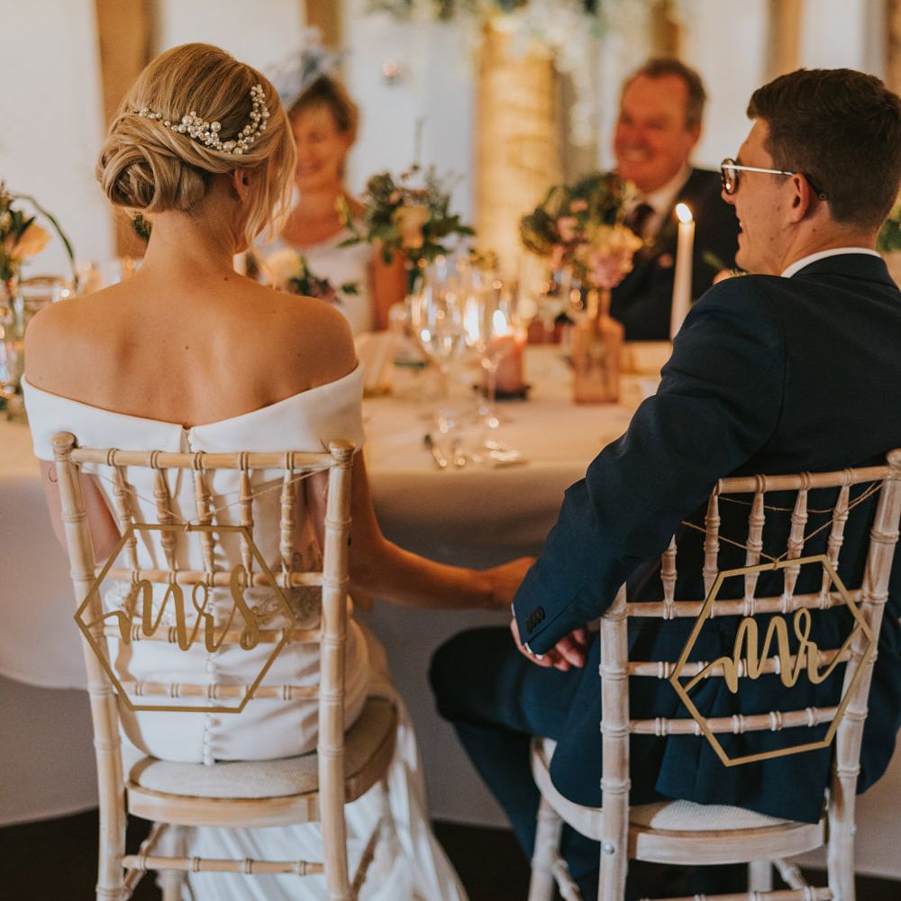 Bride & groom hold hands under the table of wedding reception 