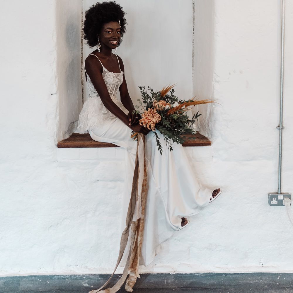 Black bride in a fitted wedding dress sitting in a wall alcove at Ponden Mill 