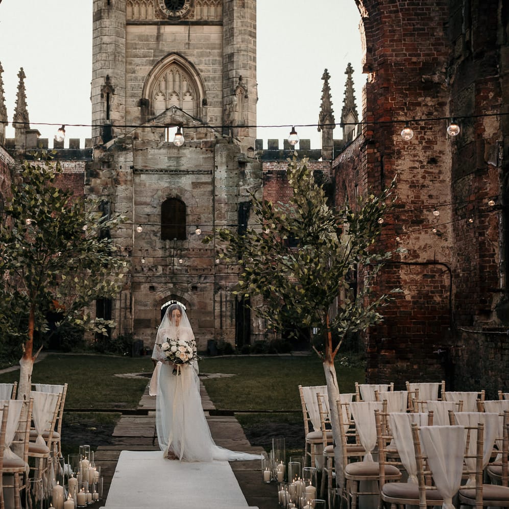 Outdoor wedding ceremony at St Lukes bombed Out Church in Liverpool with festoon lights, trees and pillar candles 