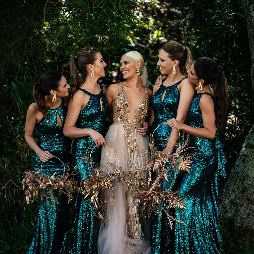 Bridal party portrait with bridesmaid in green sequin dresses holding hoop bouquets and bride in a gold wedding dress with sleek ponytail and green eyeshadow 