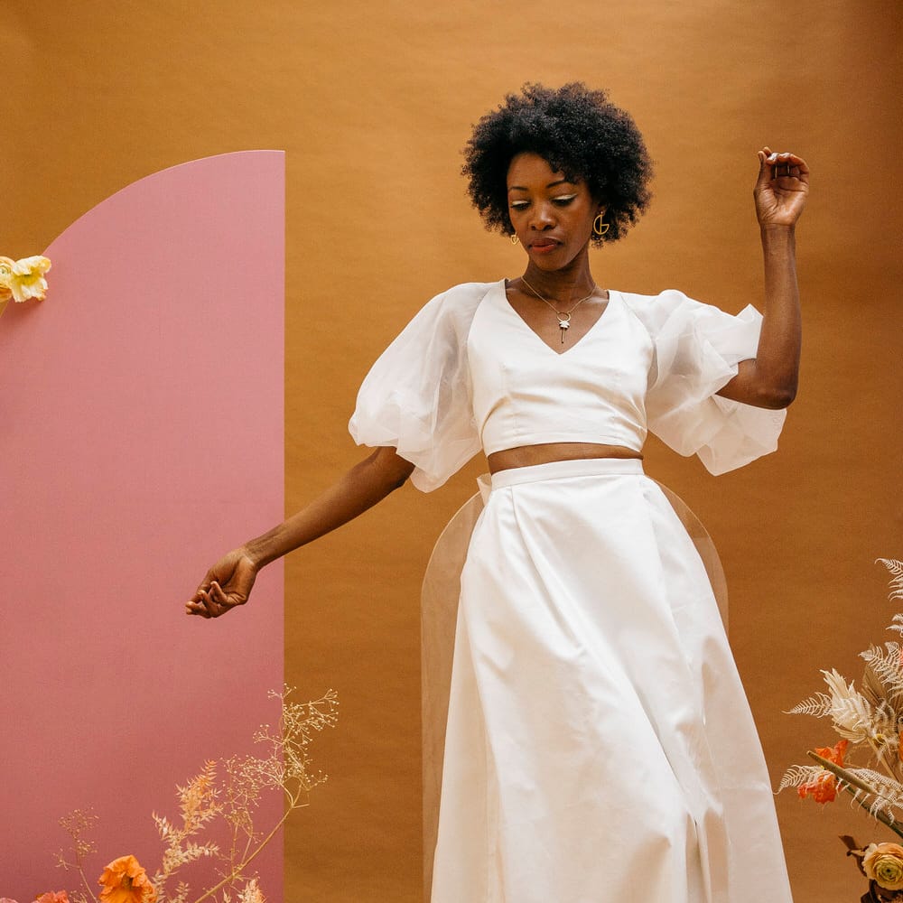 Bride wearing sleek minimal wedding separates; a puff sleeve top and long maxi skirt. Next to neutral colour dried flowers