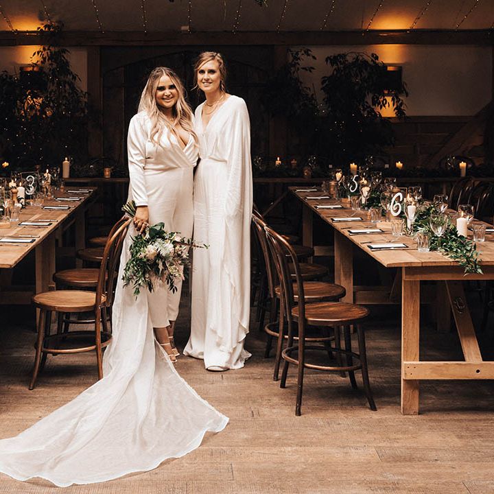 Brides stand in between wooden tables for rustic reception