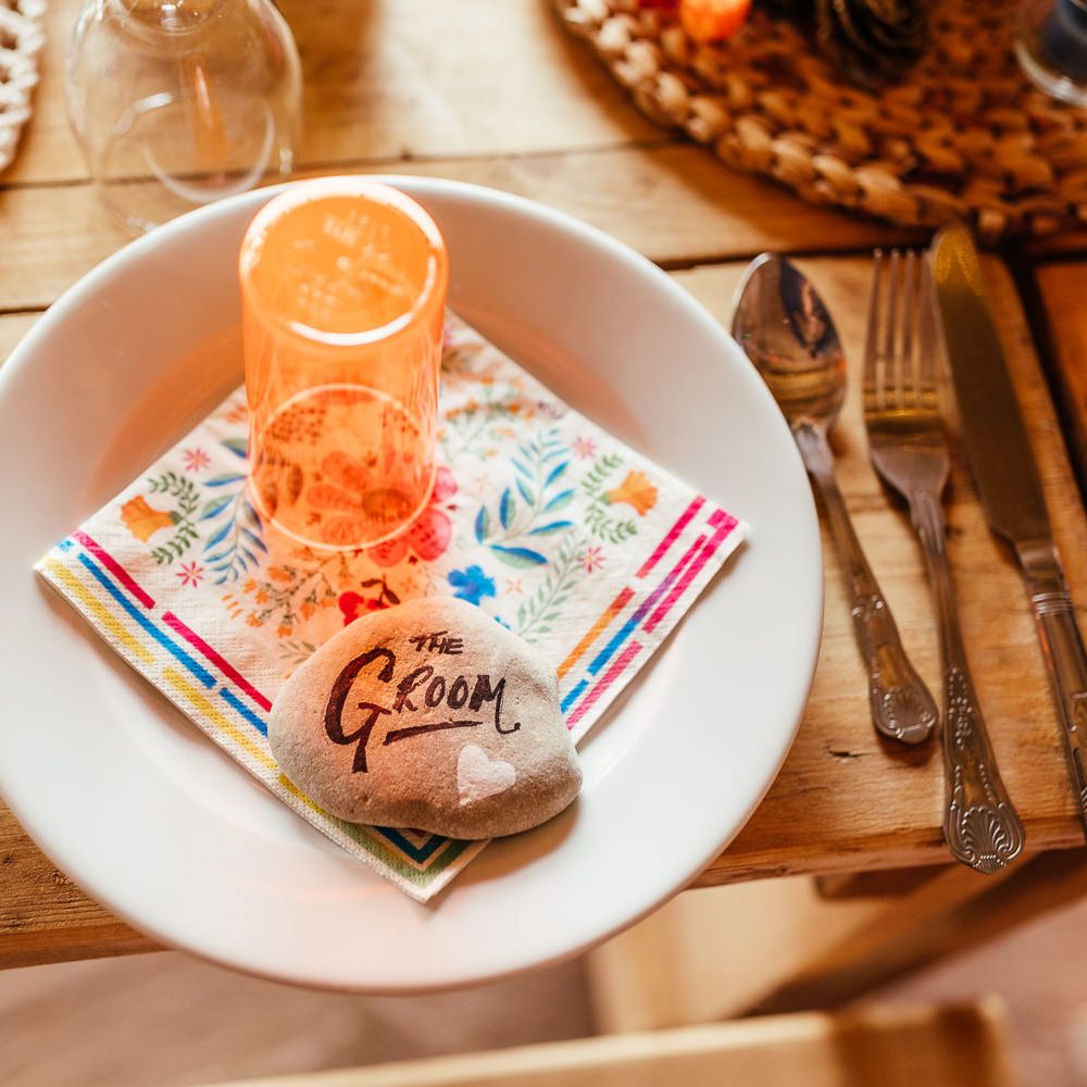 White plate with colourful napkin, orange cup and pebble table place names for rustic wedding reception