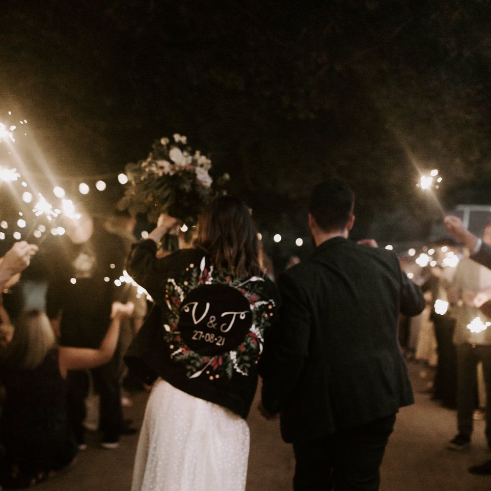 Bride & groom lean into one another as they hold sparklers with their wedding guests