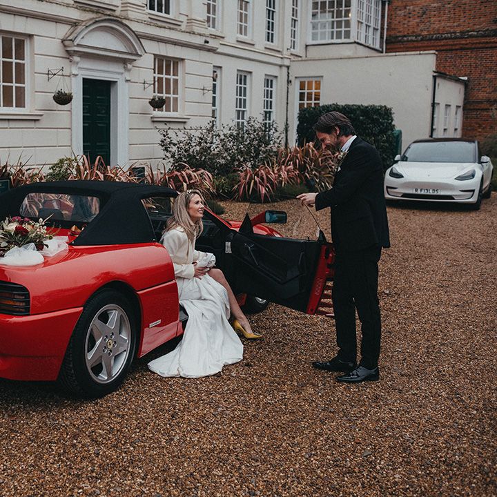 Bride sits in Ferrari as she speaks to her husband outside Gosfield Hall on their wedding day