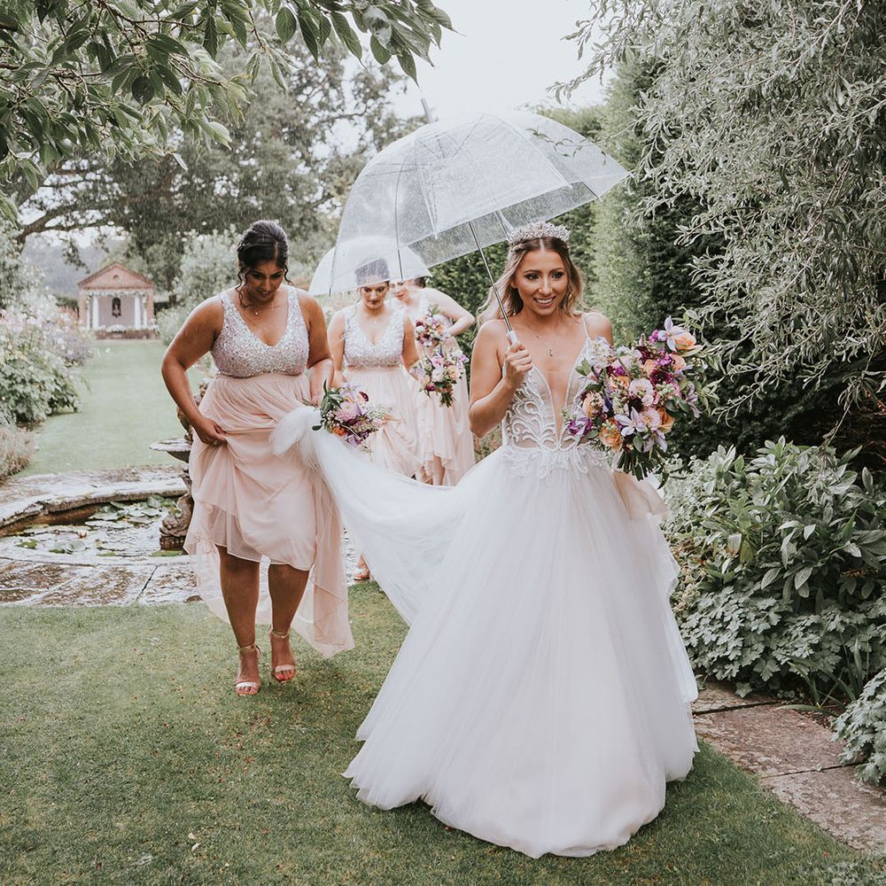 Bridesmaids walk with the bride in the rain with clear umbrellas to the wedding ceremony 