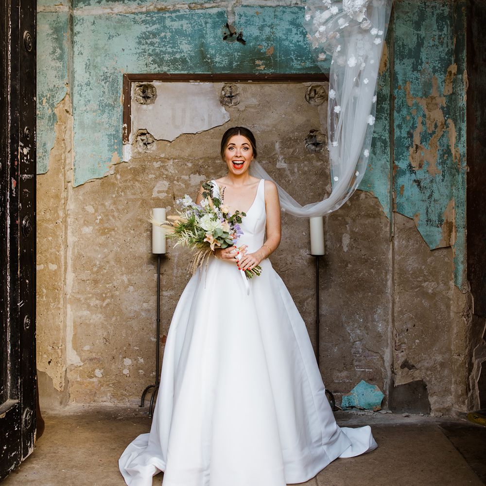 Smiling bride with large wedding bouquet and v neck gown with 3D flowers on veil