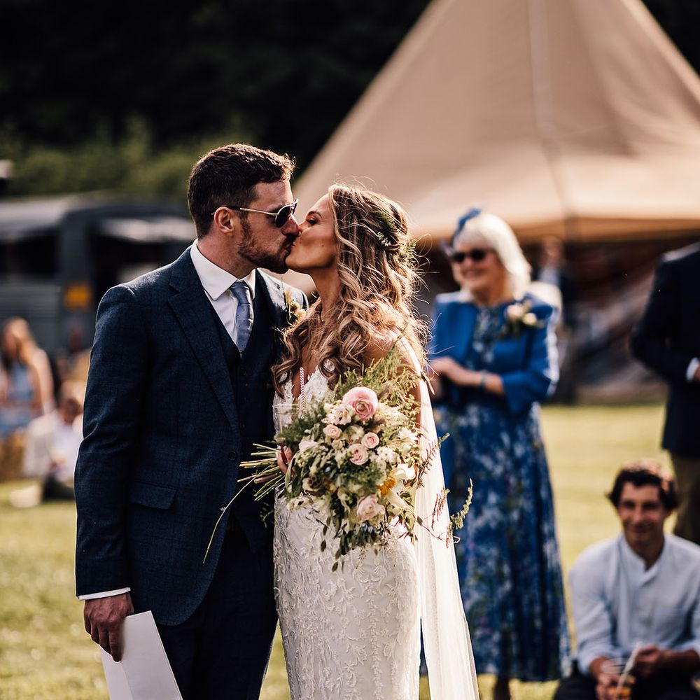 Groom in blue suit and bride in lace wedding dress share a kiss 