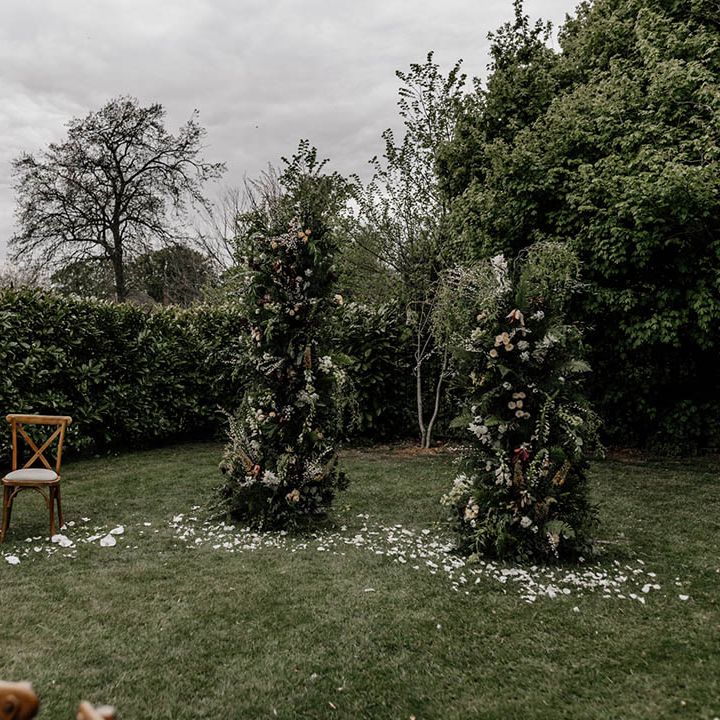 Outdoor wedding ceremony altar decor with greenery column wedding flowers and two wooden chairs