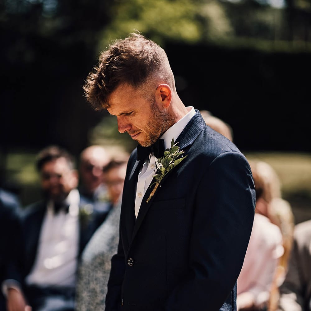 Groom waits patiently for the bride in blue tuxedo with black bow tie 
