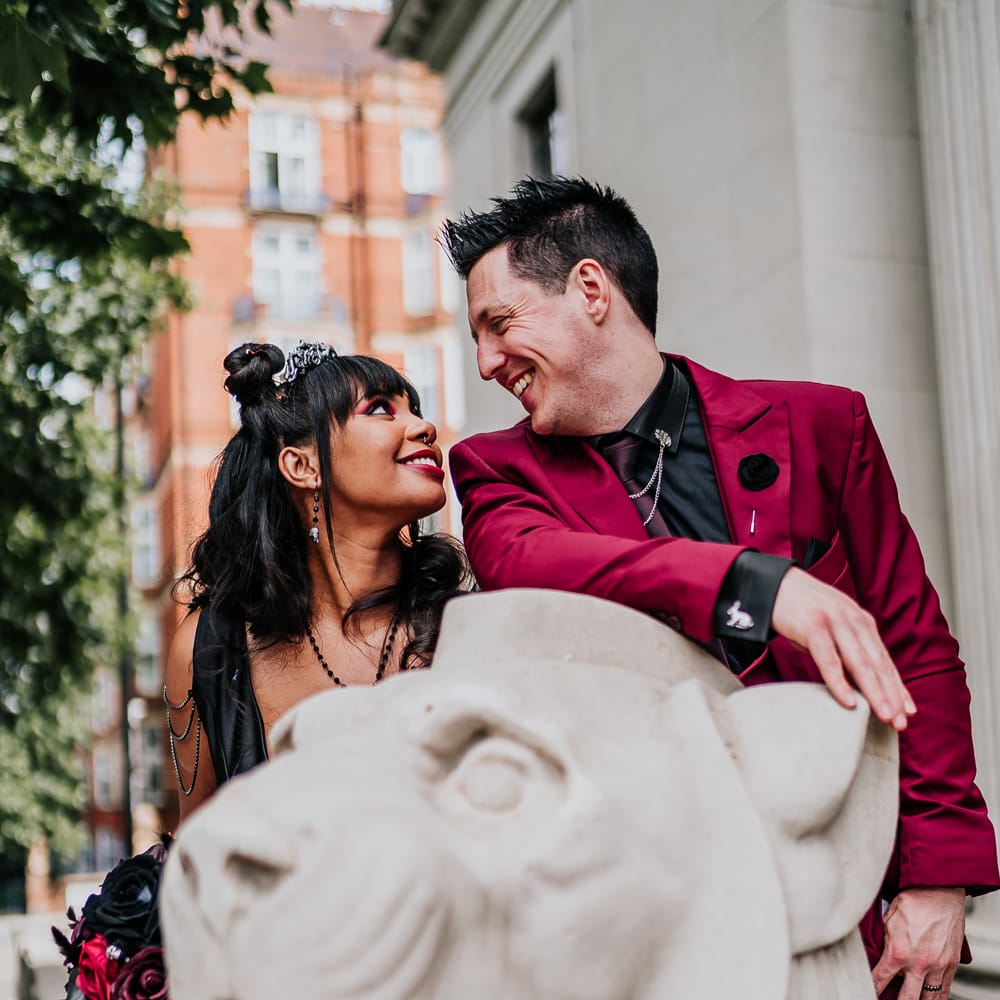 Bride & groom sit on stone lion for couples portraits on their wedding day