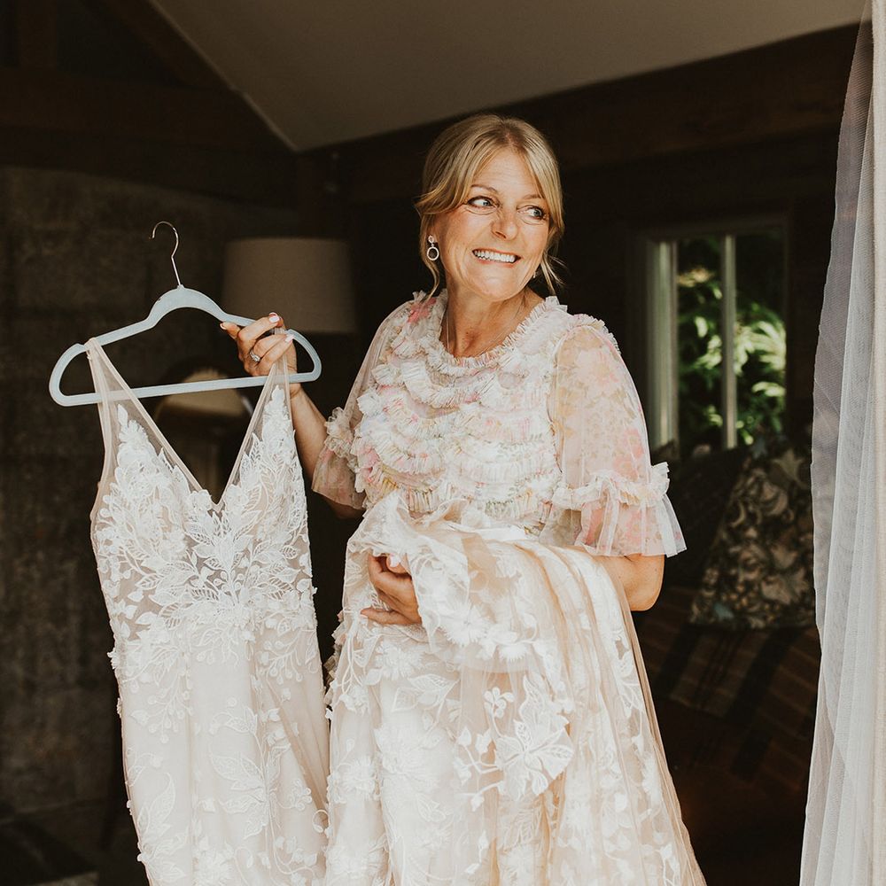 Mother of the bride in a pink floral dress holds the bride's wedding dress