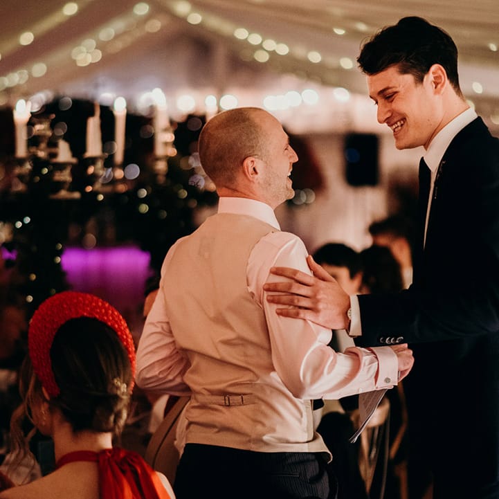 Groom in shirt and waistcoat being greeted by wedding guest in dark suit at winter wedding
