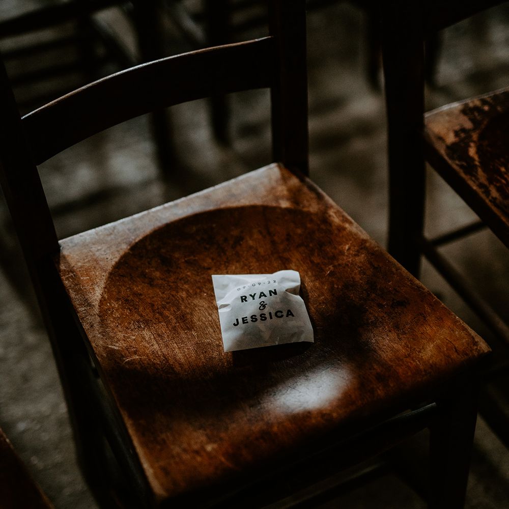 Confetti pack with the couples name on, placed on dark rustic wooden chair at alternative celestial wedding