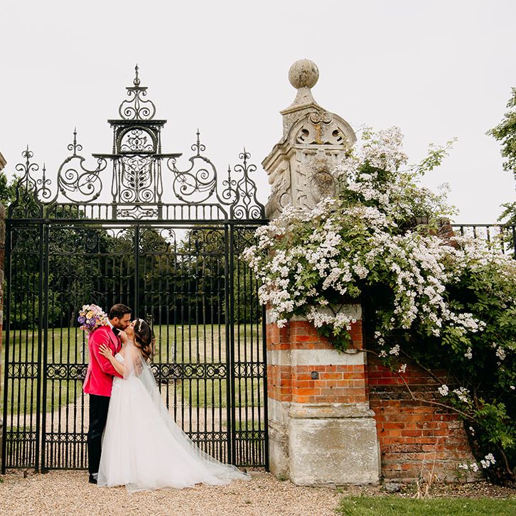 The bride and groom share a kiss as they stand together in front of the black iron gates of North Mymms Park country house 