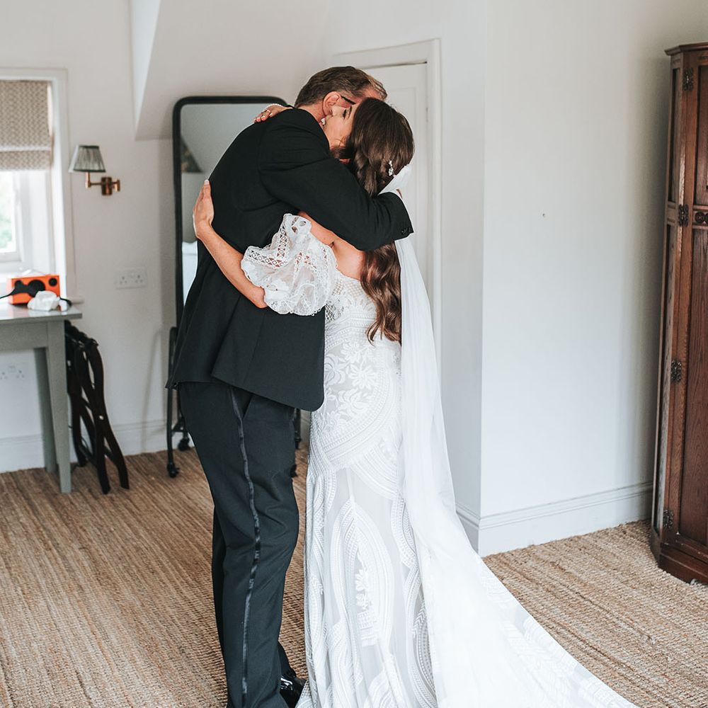 Bride in boho fitted lace wedding dress hugging her father as he sees her in her dress for the first time 