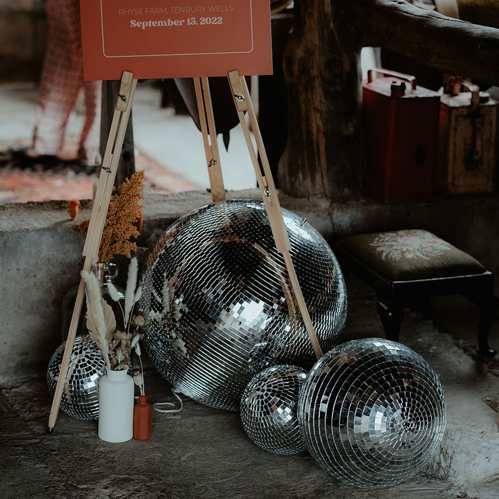 Orange and white wedding welcome sign on a wooden easel with disco ball decor and dried flowers for rustic glam wedding 