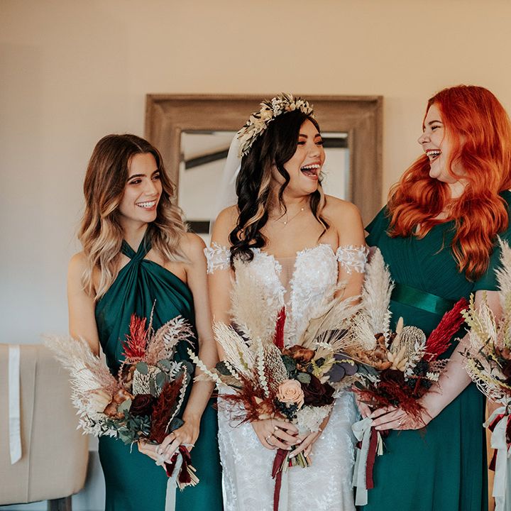 Bridesmaids in mismatched green bridesmaid dresses laughing with the bride as they get ready for the wedding at Milling Barn 