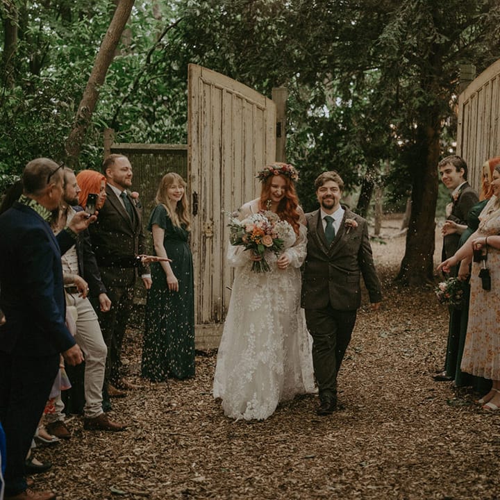 Groom in three piece suit with dark green tie has confetti moment with the bride at their outdoor woodland wedding 