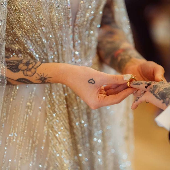 Bride in sparkly gold wedding dress giving bride golden wedding ring at Kingscote Barn Tetbury 