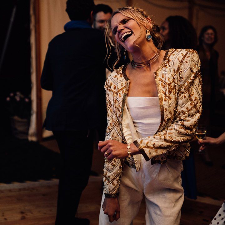 The bride in linen wedding trousers wearing a gold and white sparkly sequin beaded jacket 