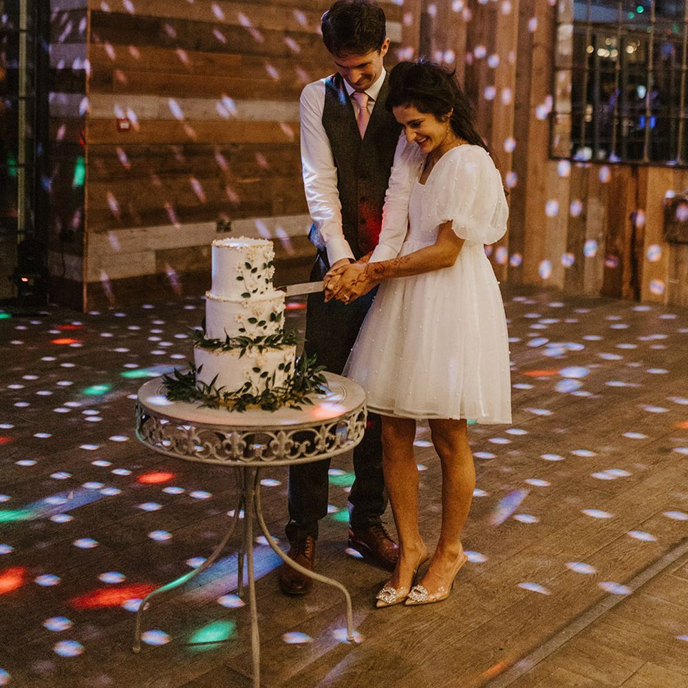Bride in short puff sleeve reception dress cuts the wedding cake with the groom 