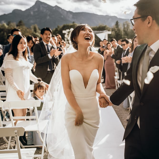 Bride in strapless Reem Acra wedding dress laughing down the aisle 