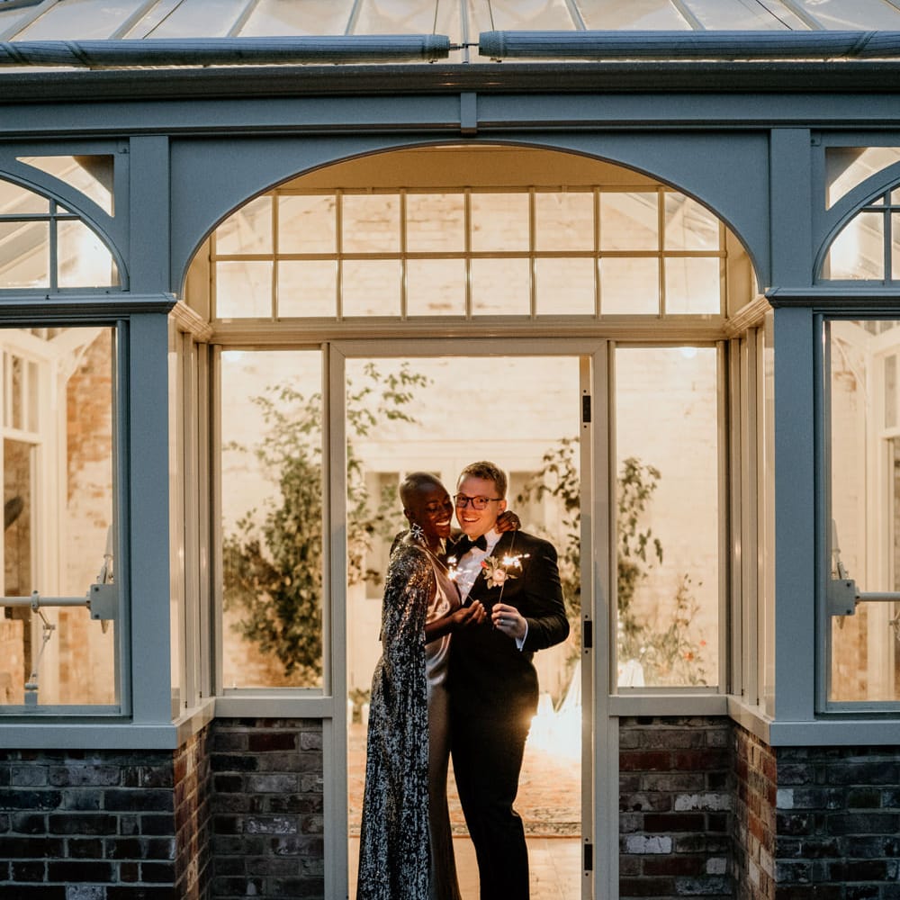 Bride and groom holding sparklers in the doorway at Our Beautiful Glasshouse in Sussex