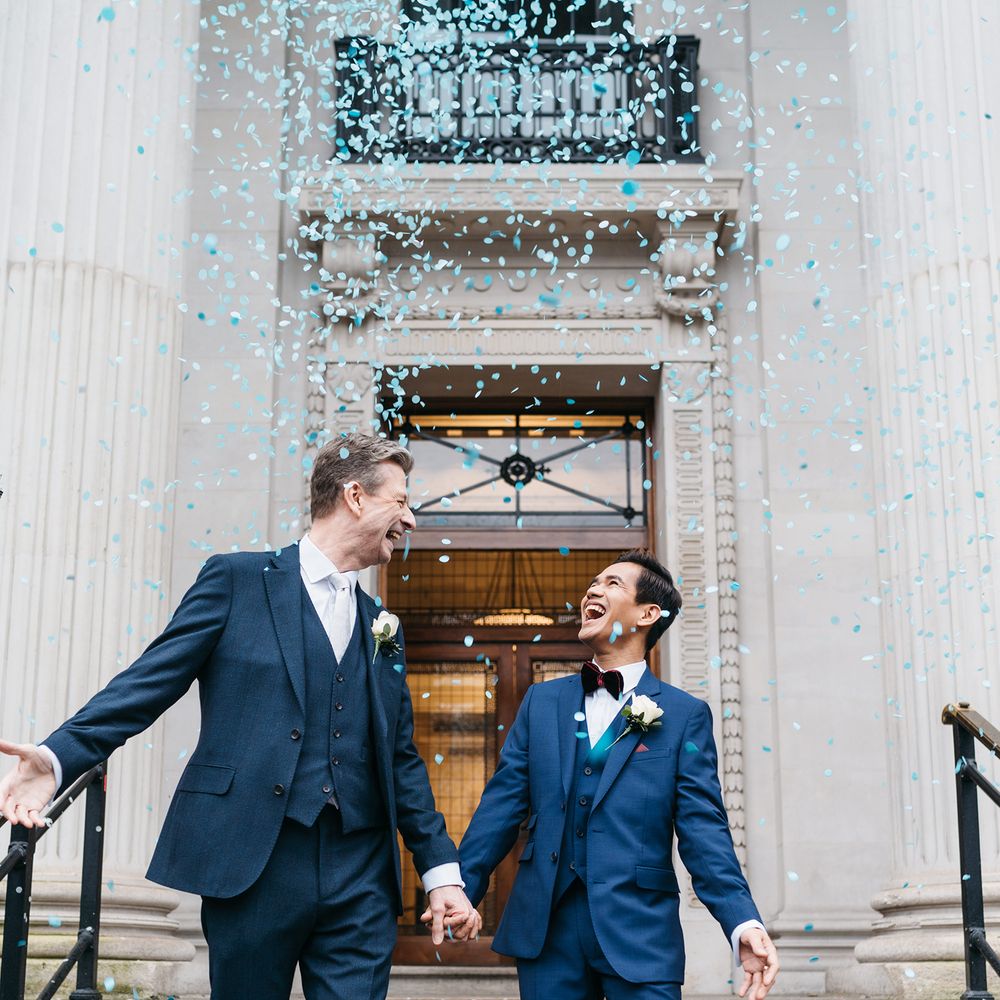 Grooms leave Old Marylebone Town Hall with blue confetti surrounding them
