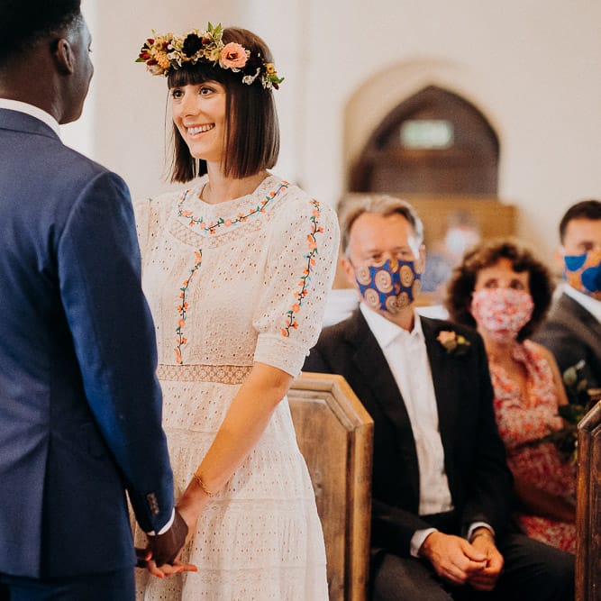 Bride in a Broderie Anglaise wedding dress with colourful embroidery detail holding hands with her groom at the altar 