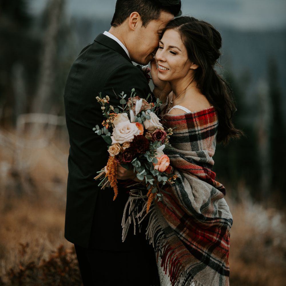 Bride & groom embrace one another whilst bride wears tartan blanket