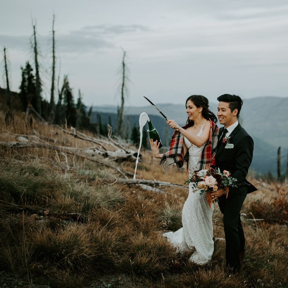 Bride sabres champagne bottle whilst groom embraces her