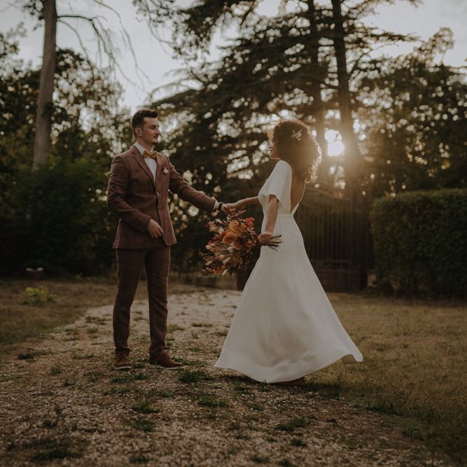 Groom in a brown wedding suit dancing at dusk with his bride in an a line wedding dress with cap sleeves and button detail
