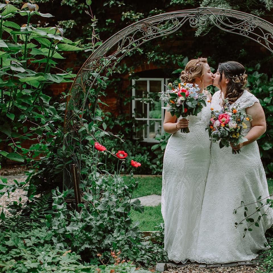 Brides kiss in gardens as they hold brightly coloured bouquets on the day of their wedding