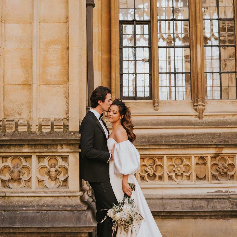 Groom in a tuxedo kissing his bride in a strapless wedding dress with puff sleeves