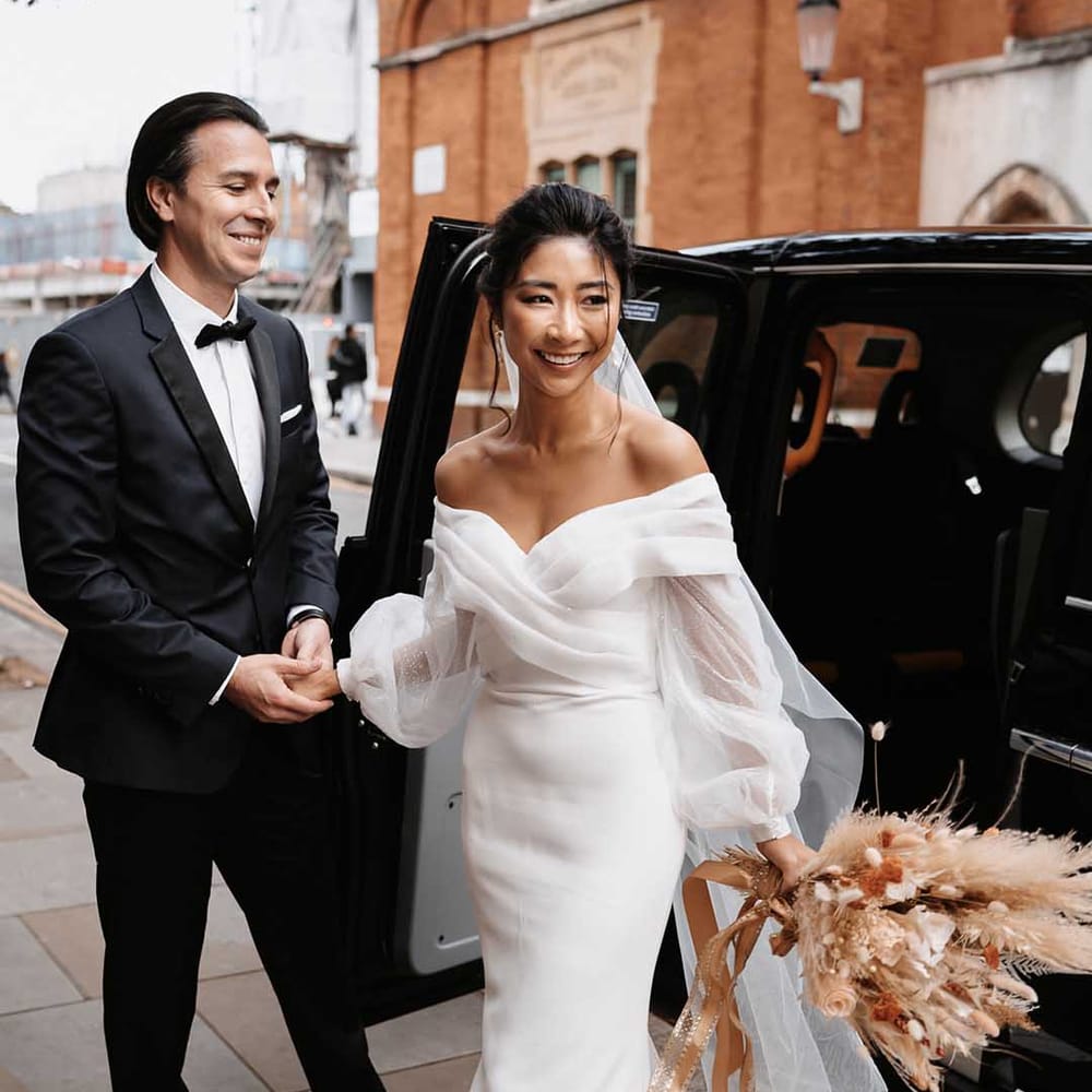 Groom in a black tux with a bow tie and Bride in simple off the shoulder wedding dress with chiffon puff sleeves 