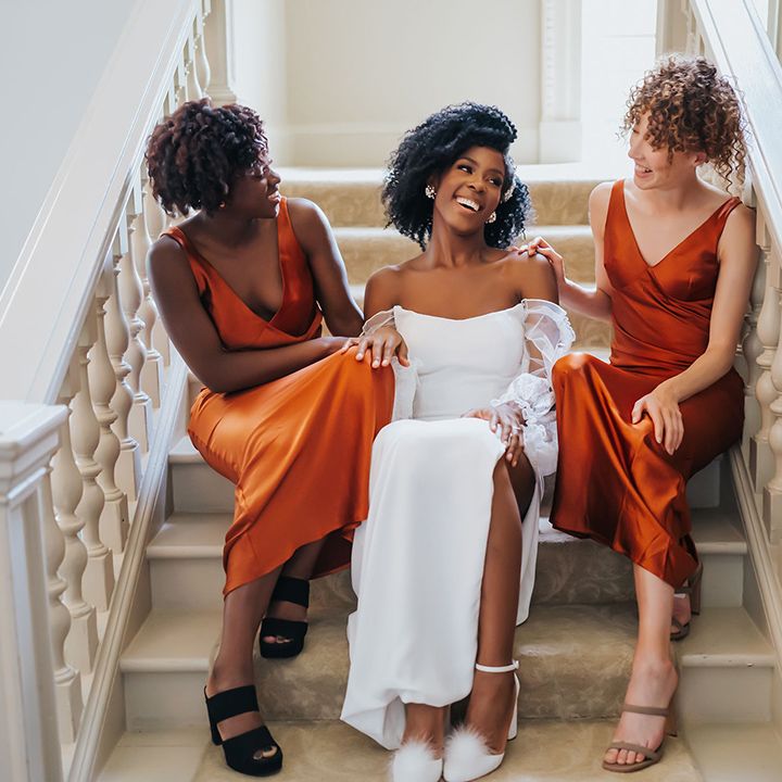 Bridal party portrait on the stairs at Modern Hall with bride in a strapless wedding dress and pom pom shoes, and bridesmaids in orange satin dresses 