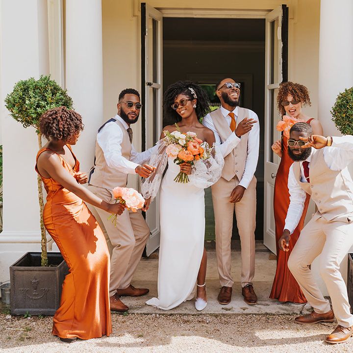 Wedding party picture with bride in a strapless wedding dress, bridesmaids in orange satin dresses and groomsmen beige suits
