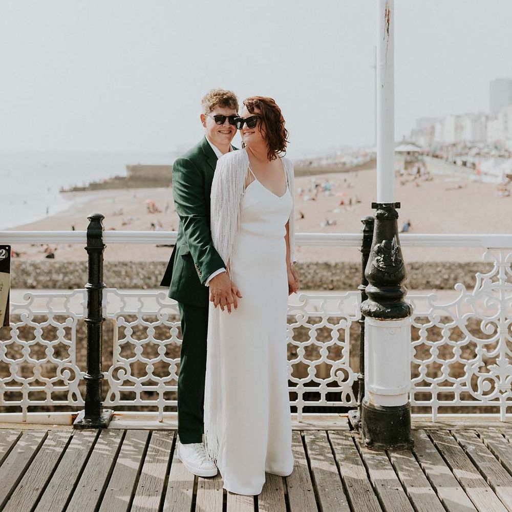 Groom stands behind groom and wraps his arms around bride on their wedding day in front of Brighton beach front