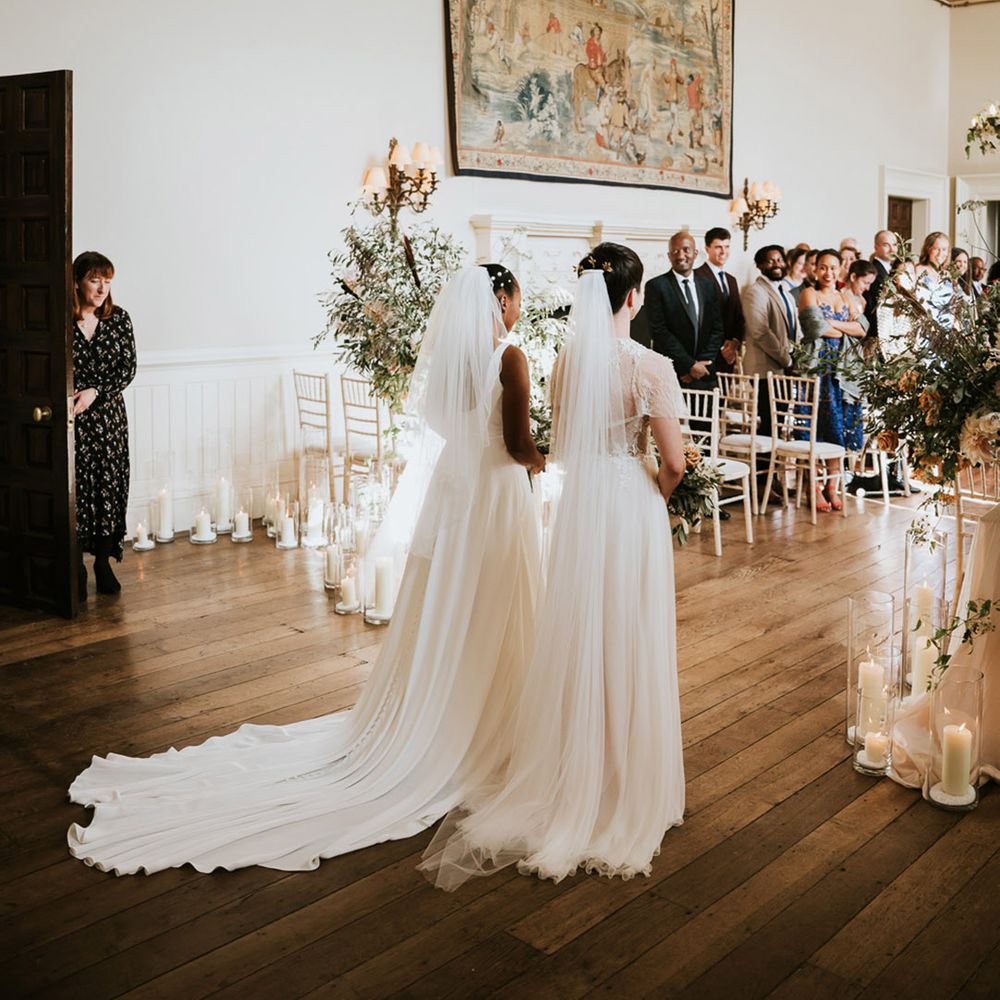 Two brides walking down the aisle together at their same sex Elmore Court wedding ceremony 