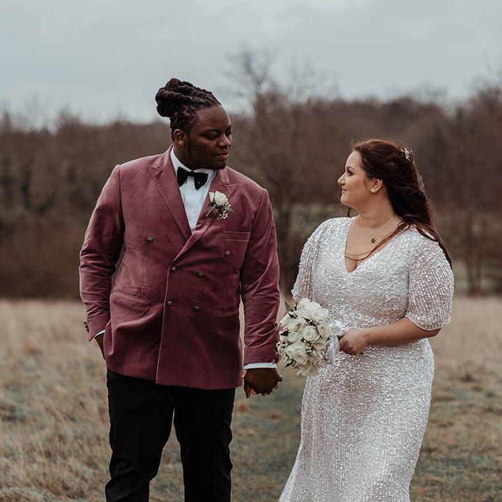 Bride & groom stand on fields on their wedding day whilst looking lovingly at one another