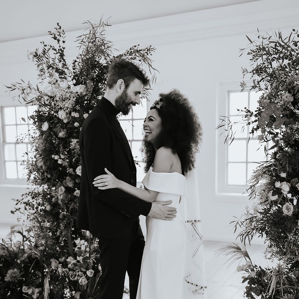 Black bride with afro hair in an off the shoulder wedding dress and appliqué patterned wedding veil 