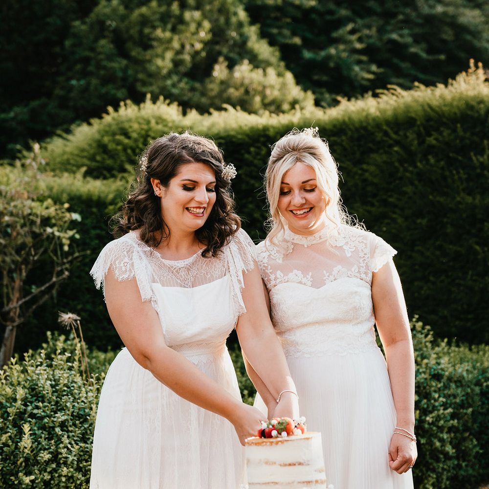 Brides cut their two tier semi naked white frosted wedding cake together with summer berries and gypsophila decor