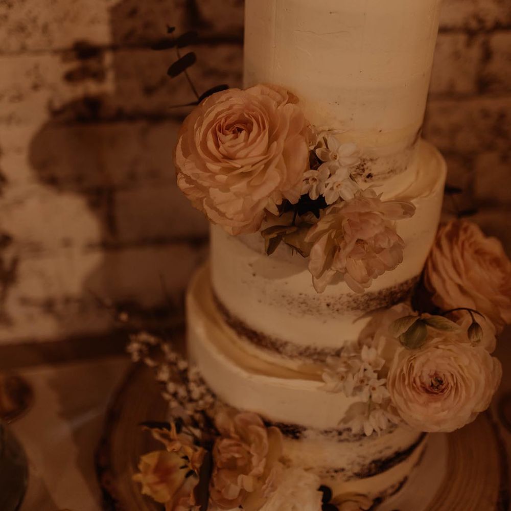 Semi naked three tier white frosted wedding cake with pink and whit flower decorations and wooden heart cake topper with personalised details 