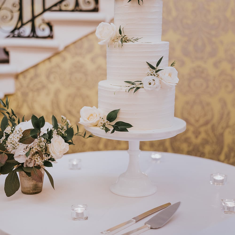 Three tier white frosted wedding cake with white roses and foliage 