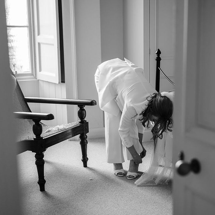 Bride puts on her shoes whilst wearing bridal suit on her wedding day